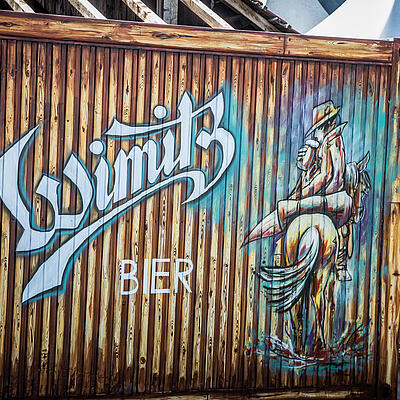 Bemalte Holzwand mit Wimitzbräu-Schriftzug und Cowboy-Figur – Symbol der Privatbrauerei Wimitzbräu in Kärnten.