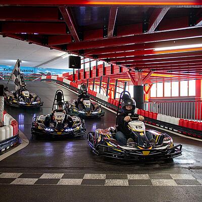 Mehrere Personen fahren mit E-Karts auf der Indoor-Kartbahn Rosental durch eine Kurve.
