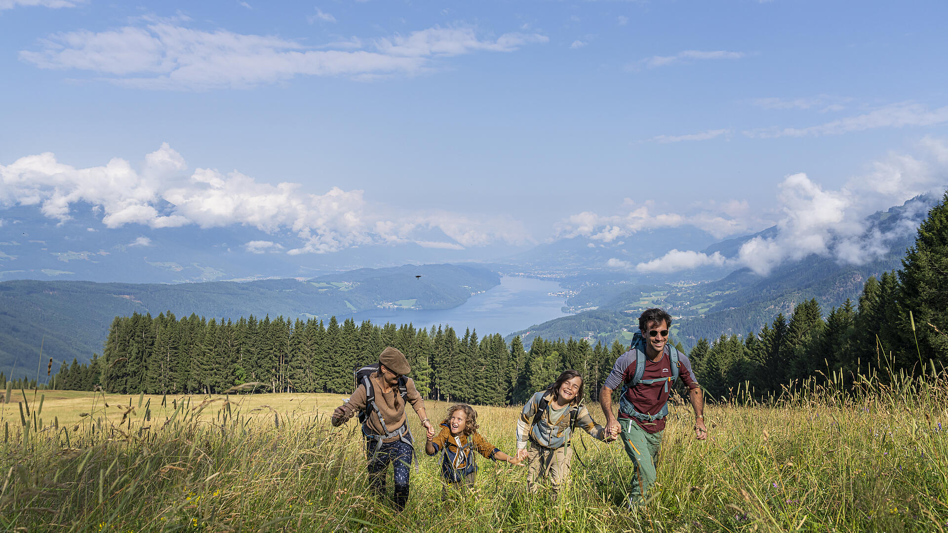 Wandergenuss mit der Familie – Natur erleben am Millstätter See Vierköpfige Familie wandert durch eine blühende Bergwiese mit Blick auf den Millstätter See