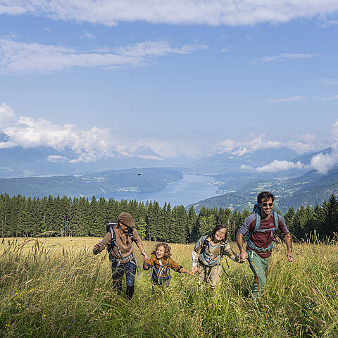Wandergenuss mit der Familie – Natur erleben am Millstätter See Vierköpfige Familie wandert durch eine blühende Bergwiese mit Blick auf den Millstätter See