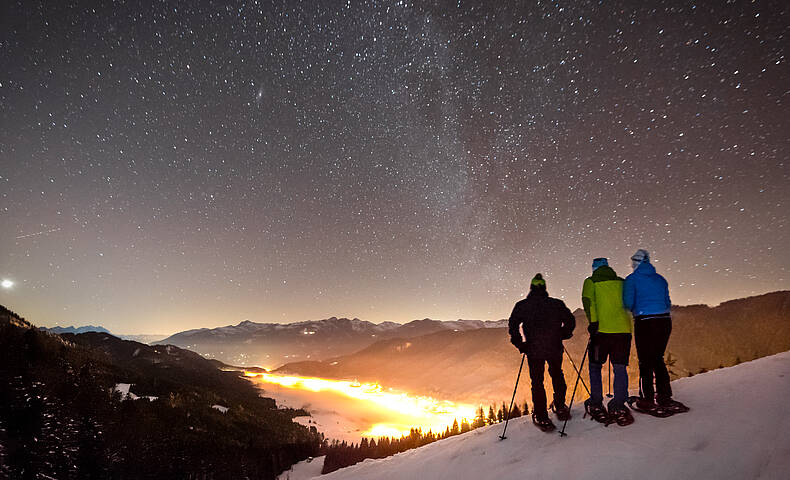 Winterwanderer genießen den Sternenhimmel über dem Weissensee in verschneiter Wintelandschaft.