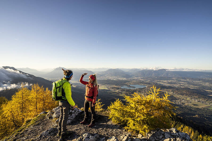 Zwei Wandernde auf der Ferlacher Spitze mit Blick über die Berg- und Seenlandschaft der Region Villach.