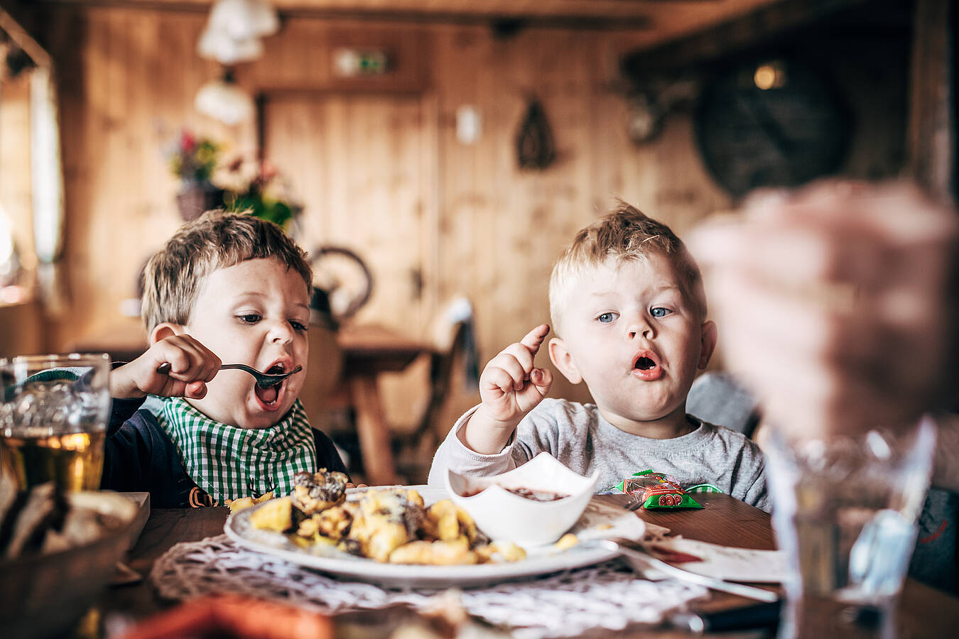 Zwei Kinder sitzen in einer gemütlichen Holzhütte am Tisch und essen gemeinsam.