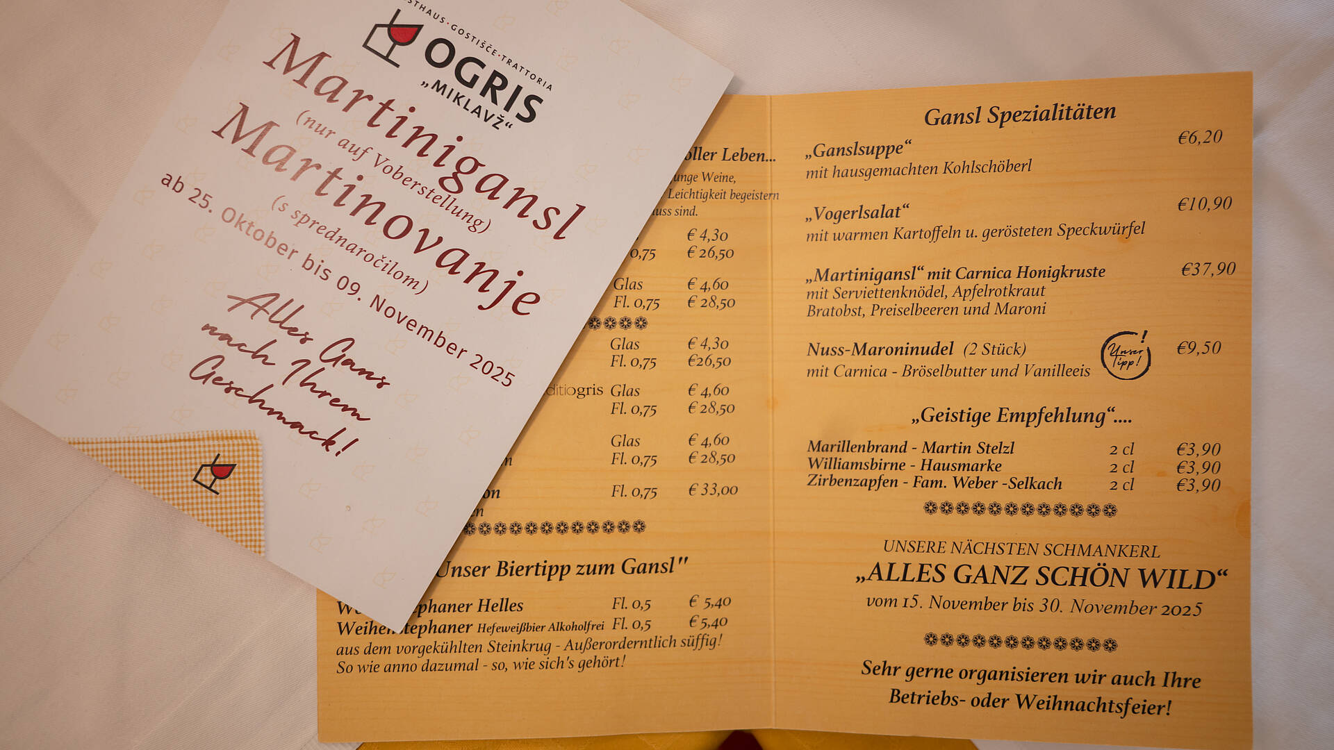 Gedruckter Flyer und geöffnete Menükarte mit Ganslzeit-Spezialitäten im Gasthaus Ogris. Aufgelistet sind Suppen, Hauptspeisen wie Martinigansl mit Honigkruste und Desserts sowie Getränkeempfehlungen.