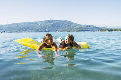 Zwei Mädchen genießen sommerlichen Badespaß mit Luftmatratzen im Wörthersee.