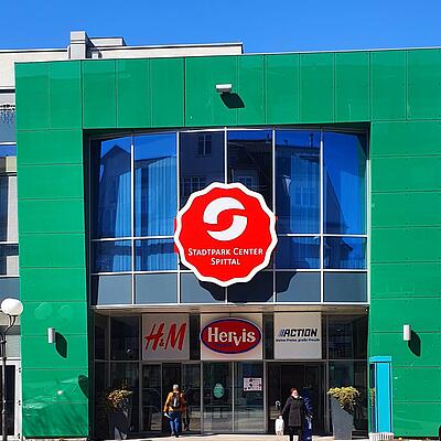 Haupteingang des Stadtpark Center Spittal mit Logos von H&M, Hervis und Action.