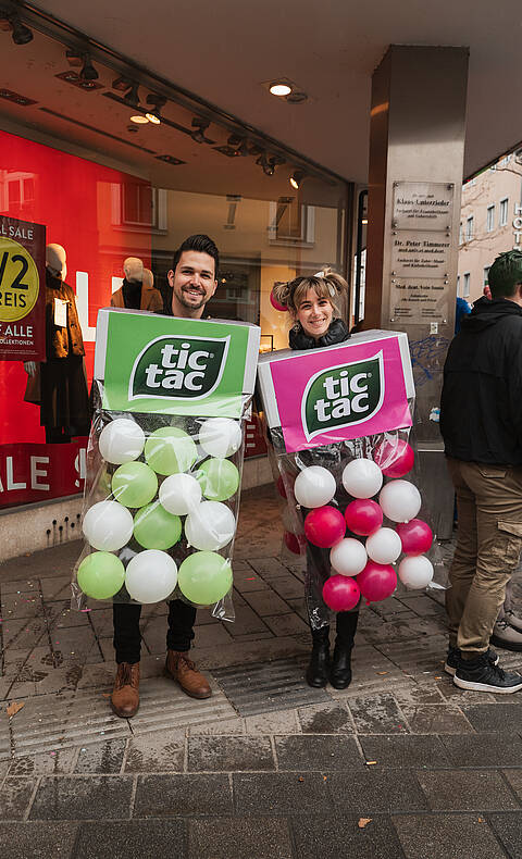 Zwei Personen in bunten Süßigkeiten-Kostümen stehen beim Villacher Fasching in der Innenstadt von Villach.