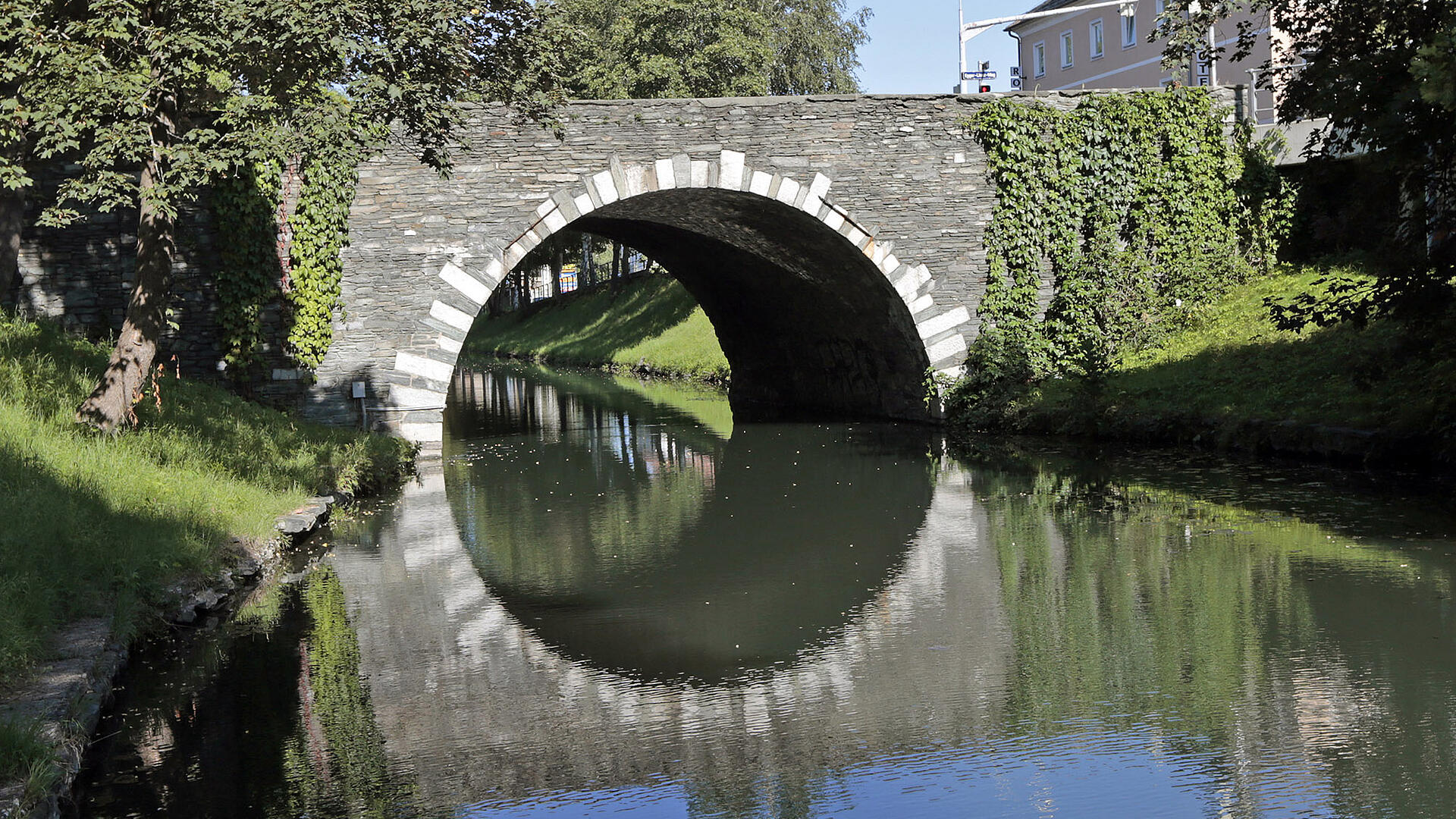 Steinerne Brücke am Lendkanal in Klagenfurt Steinerne Brücke in Klagenfurt über den Lendkanal, umgeben von Bäumen und begrünten Ufermauern.