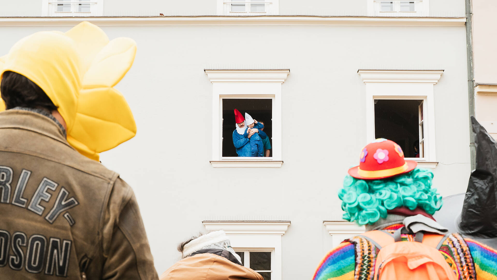 Als Zwerge verkleidete Personen beobachten den Villacher Fasching aus einem Fenster in der Innenstadt.
