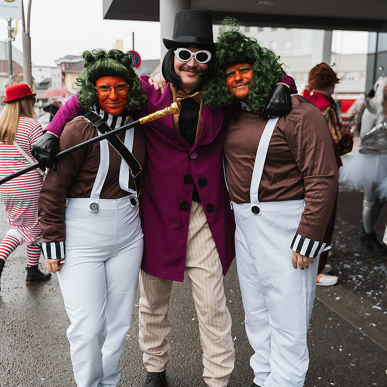 Drei verkleidete Personen posieren beim Villacher Fasching auf einer Straße in Villach.