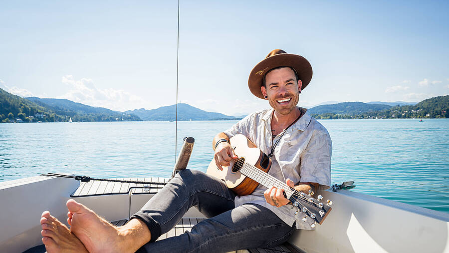 Auf einem kleinen Boot entsteht ein musikalischer Augenblick, begleitet vom klaren Wasser des Wörthersees und einer ruhigen Naturkulisse. Ein Bild, das sommerliche Freiheit und künstlerische Inspiration vereint.
