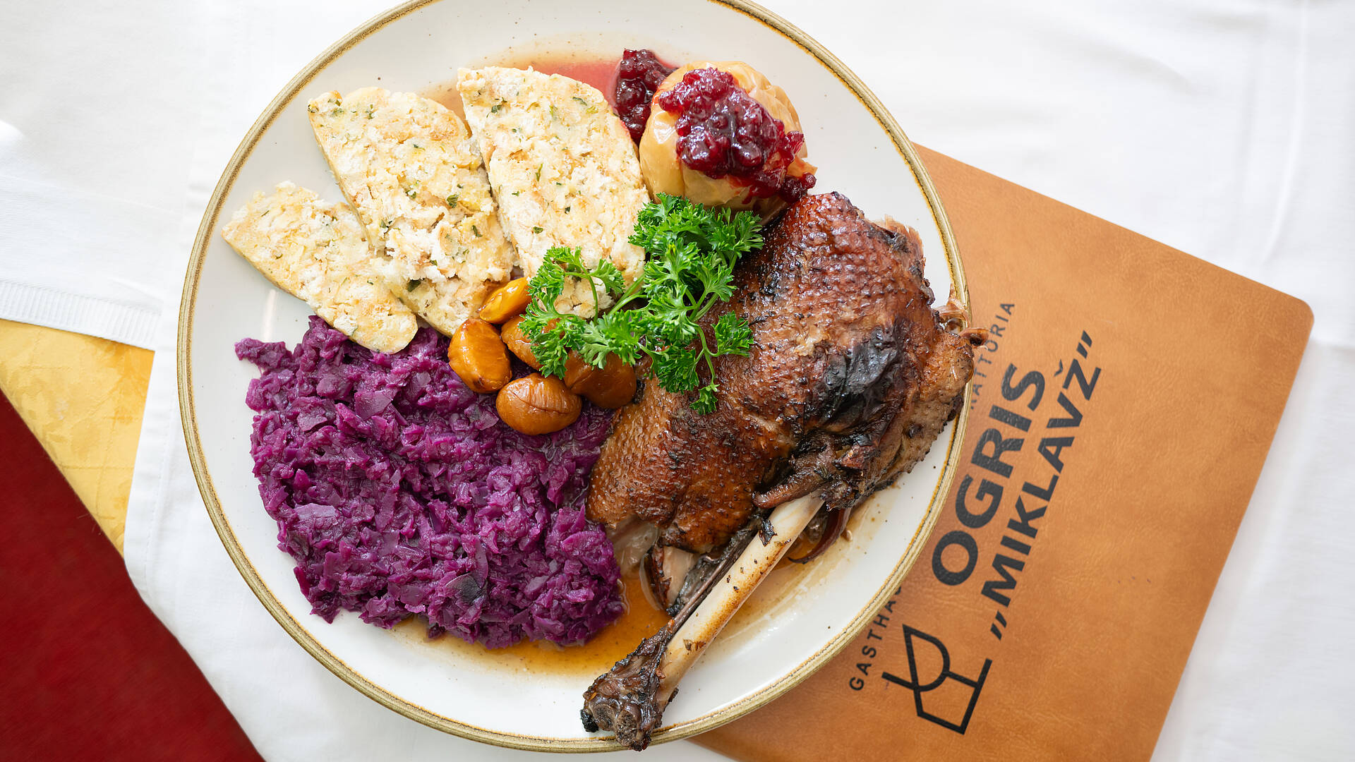 Ein herbstliches Martinigansl-Gericht im Gasthaus Ogris in Ludmannsdorf: knusprige Gans mit Apfelrotkraut, Serviettenknödel, Maroni, Bratobst und Preiselbeeren auf einem weißen Teller