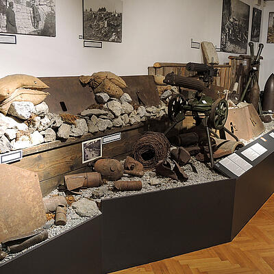 Ausstellungsraum im Museum 1915–1918 mit Fundstücken aus dem Ersten Weltkrieg, darunter Waffen, Munition, Sandsäcke, Stahlplatten und historische Fotos