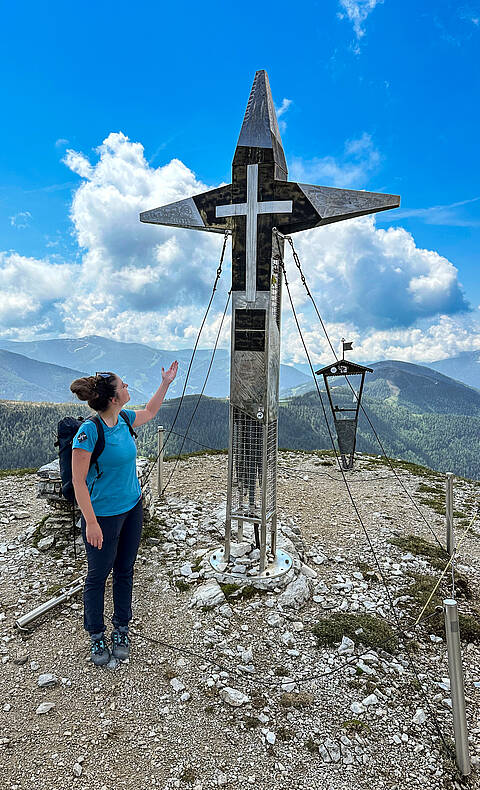 Eine Wanderin am Gipfelkreuz am Predigerstuhl am Nockberge Trail.