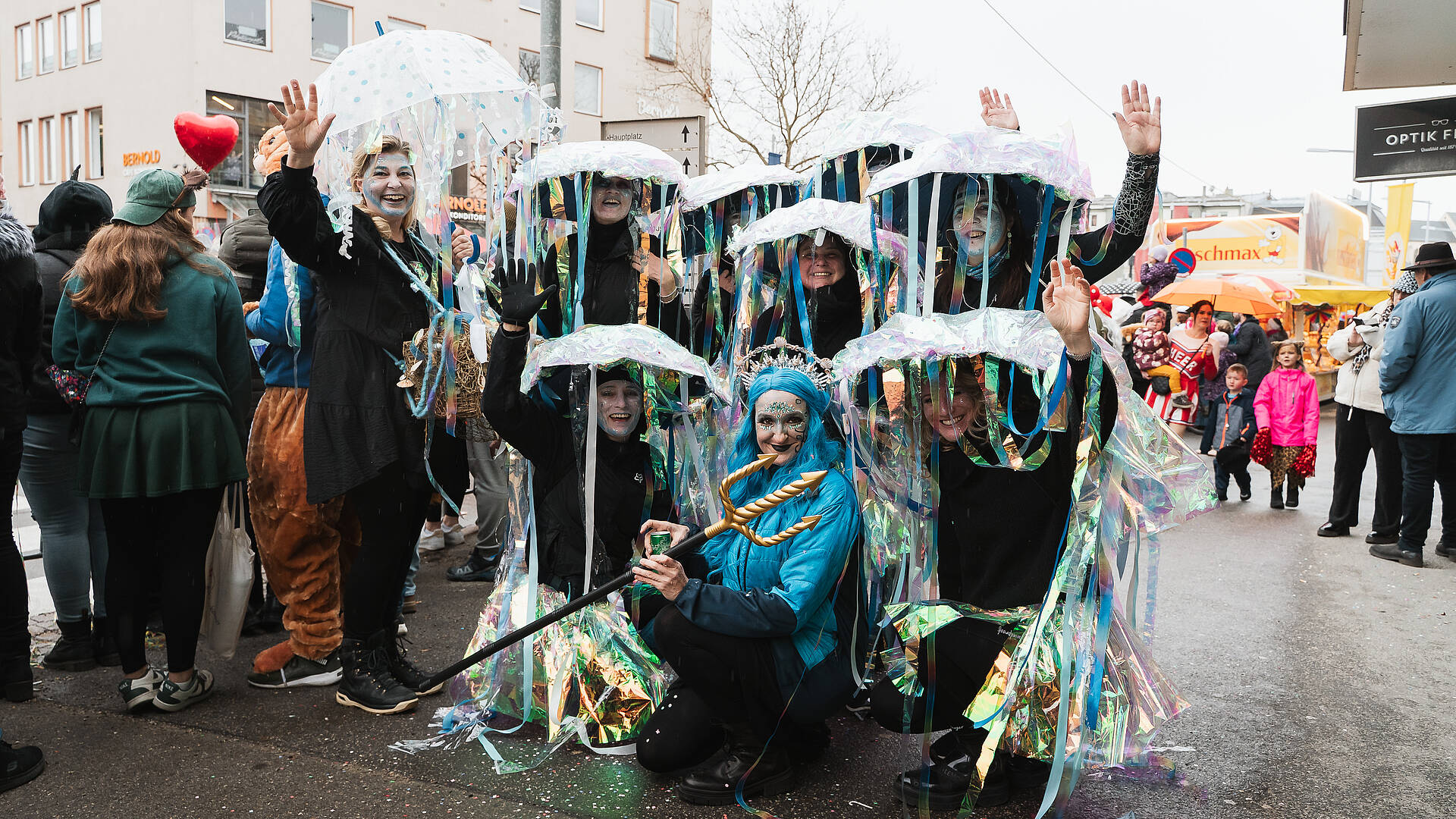 Gruppe von verkleideten Personen in schimmernden Meereskostümen mit transparenten Schirmen feiert beim Villacher Fasching in der Innenstadt von Villach.