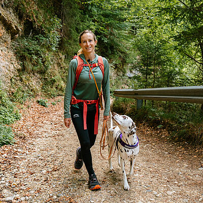 Frau mit Rucksack wandert auf dem Waldweg am Kitzelberg, neben ihr ein Dalmatiner an der Leine, der sie anschaut.