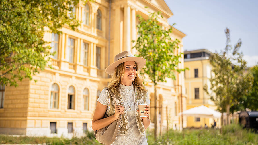 Eine Person steht vor einem eindrucksvollen historischen Gebäude in Kärnten, umgeben von grüner Parklandschaft und warmem Sommerlicht