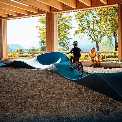Kinder fahren mit Helmen auf einem Indoor-Pumptrack in Drobollach am Faaker See.