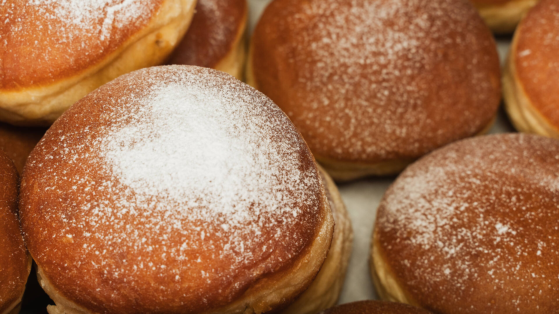 Mehrere frisch gebackene Faschingskrapfen mit Staubzucker liegen dicht nebeneinander auf einem Blech.