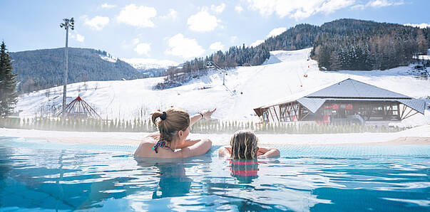 Zwei Personen im Außenpool vom Römerbad in Bad Kleinkirchheim mit Blick auf die Scheepiste