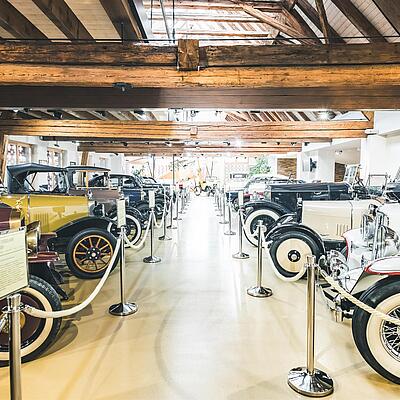 Innenansicht des Salvator Automuseums in St. Salvator mit einer Reihe restaurierter Oldtimer und historischen Automobilen unter einem rustikalen Holzdach.