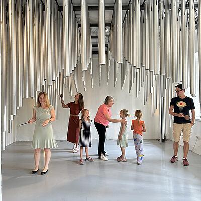 Kinder und Erwachsene spielen gemeinsam auf großen Metallröhren in einer Klanginstallation im Haus des Staunens.