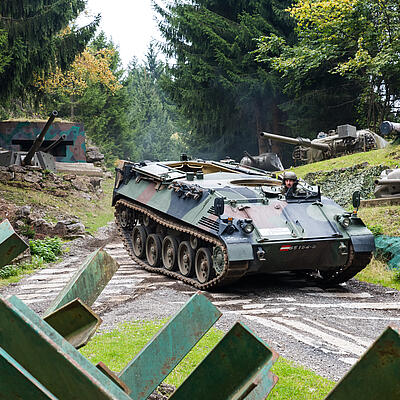 Panzer fährt durch das Außengelände des Bunkermuseums am Wurzenpass, umgeben von militärischen Relikten und Wald.