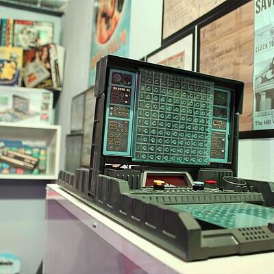 Retro-Spielkonsole im Gamingmuseum Döbriach mit buntem Spielfeld, umgeben von Regalen voller Spieleklassiker und Gaming-Exponate.