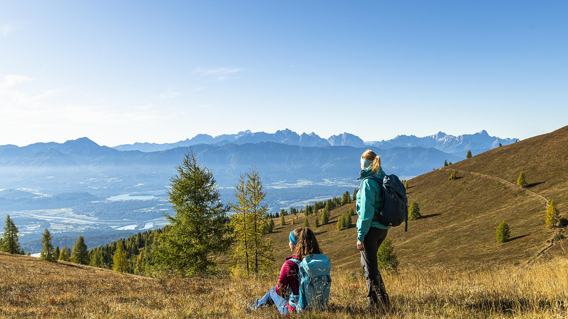 Wandern mit Weitblick – Herbstzauber auf der Gerlitzen Alpe Zwei Wanderinnen mit Rucksäcken genießen den Weitblick von der Gerlitzen Alpe über herbstliche Landschaft und ferne Berge.