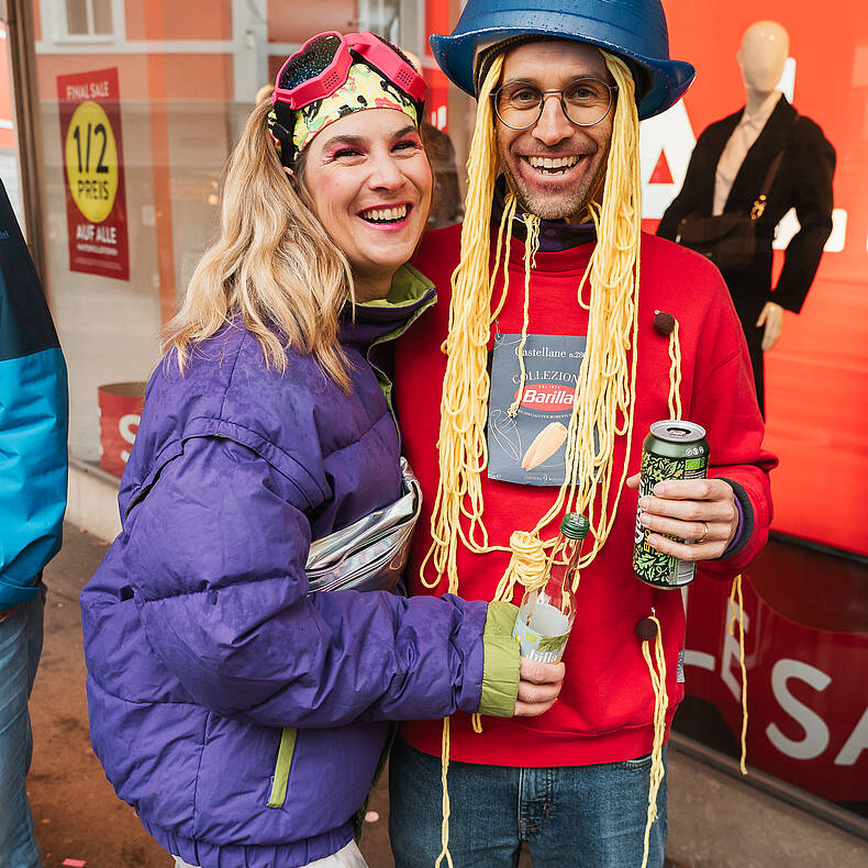Zwei verkleidete Personen lachen und posieren beim Villacher Fasching in der Innenstadt.