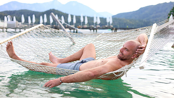 Mann liegt in Hängematte am Klopeiner See und genießt die Auszeit in Kärnten