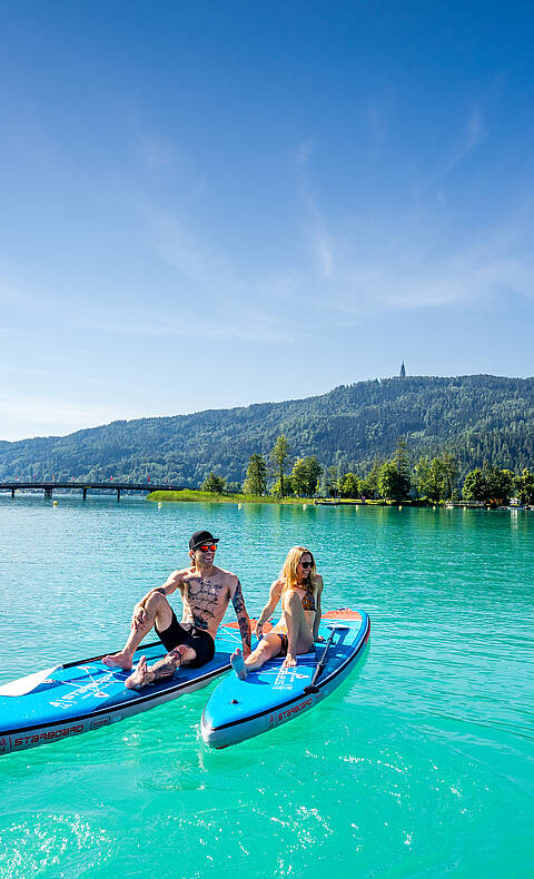 Mann und Frau sitzen am Stand Up Paddle und genießen einen schönen Sommertag am Wörthersee