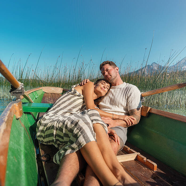 Frau und Mann liegen im Ruderboot und genießen die Sonne