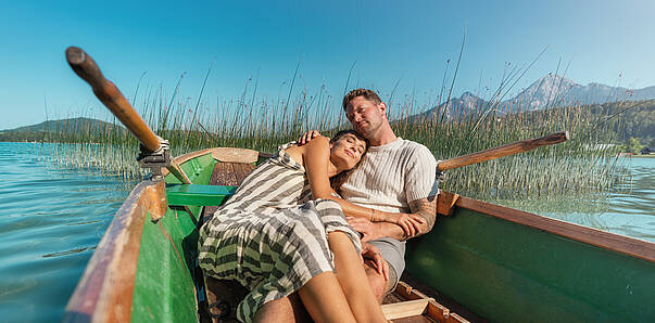 Frau und Mann liegen im Ruderboot und genießen die Sonne