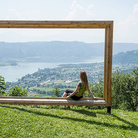 Eine Frau macht eine Pause beim Bilderrahmen am Ossiachberg